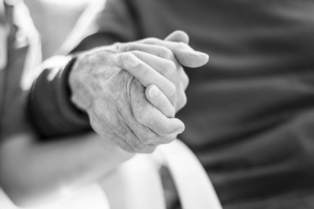 Black-and-white close-up of two elderly hands clasped together, symbolizing enduring love, commitment, and the passage of time